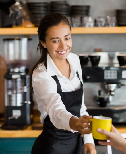 a woman wearing a black apron handing a yellow cup to a person