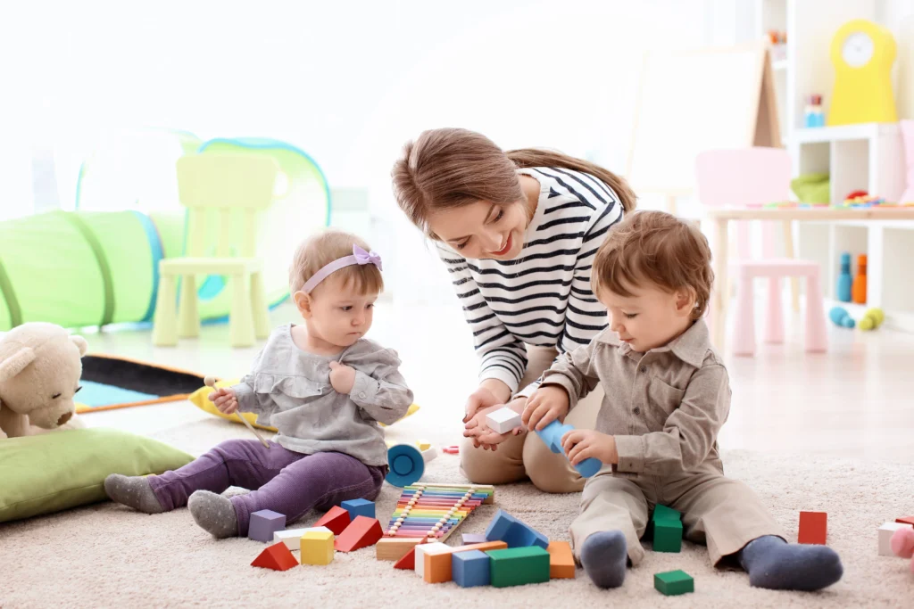 Adult playing with 2 toddlers on the ground